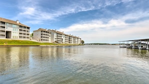 A waterfront hotel with multiple floors, a grassy area in front, and a dock with boats. - Lake-view Patio, Pool Access! Regatta Bay Condo (Lake Ozark)