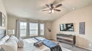 Une chambre à coucher comprenant un lit, une commode, un ventilateur de plafond et un téléviseur fixé au mur.