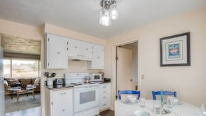 Una cocina compacta con armarios blancos, microondas, estufa y comedor con mesa para cuatro.