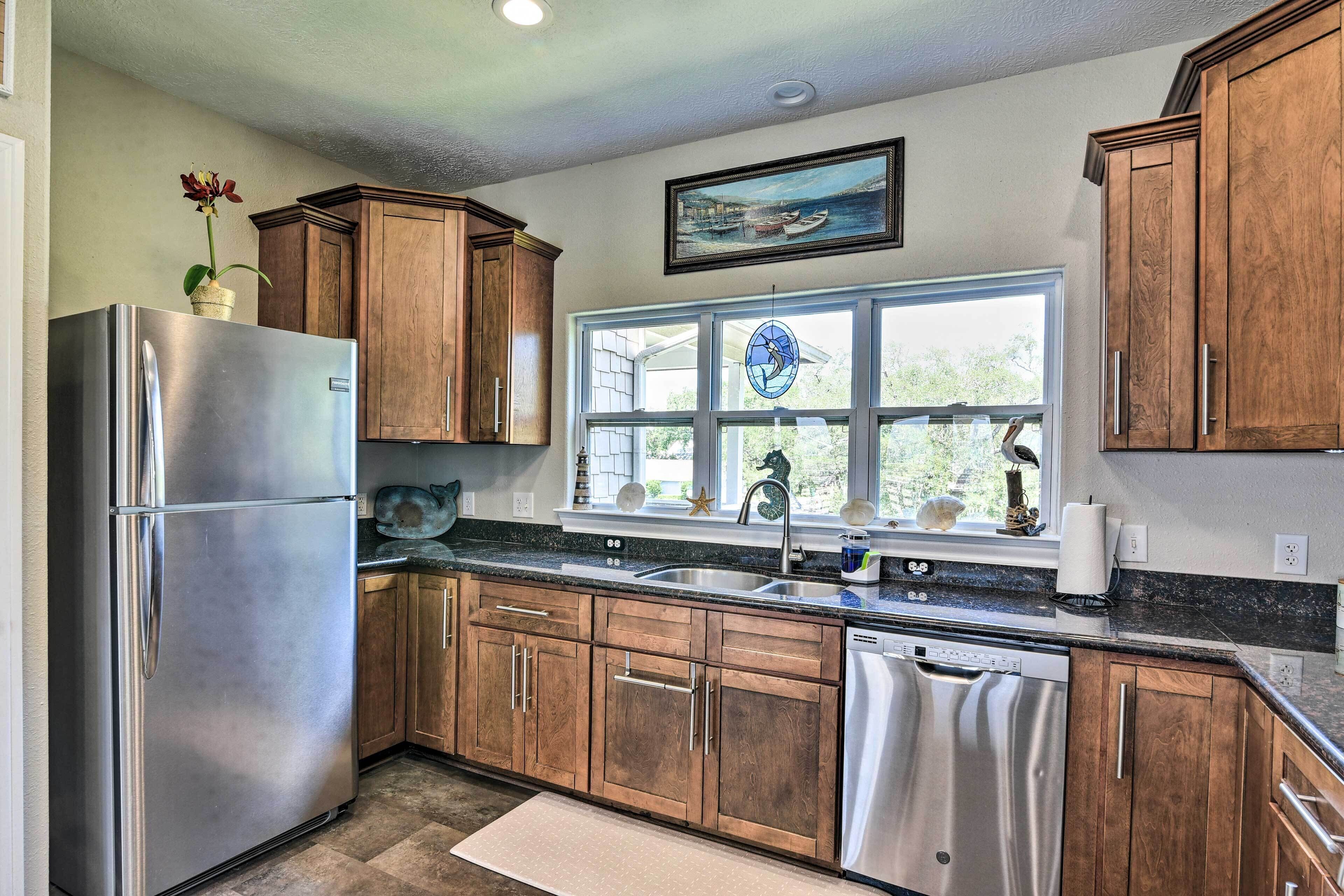 A modern kitchen with wooden cabinets, stainless steel appliances, and a large window with a view of the outdoors.