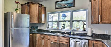 A modern kitchen with wooden cabinets, stainless steel appliances, and a large window with a view of the outdoors.