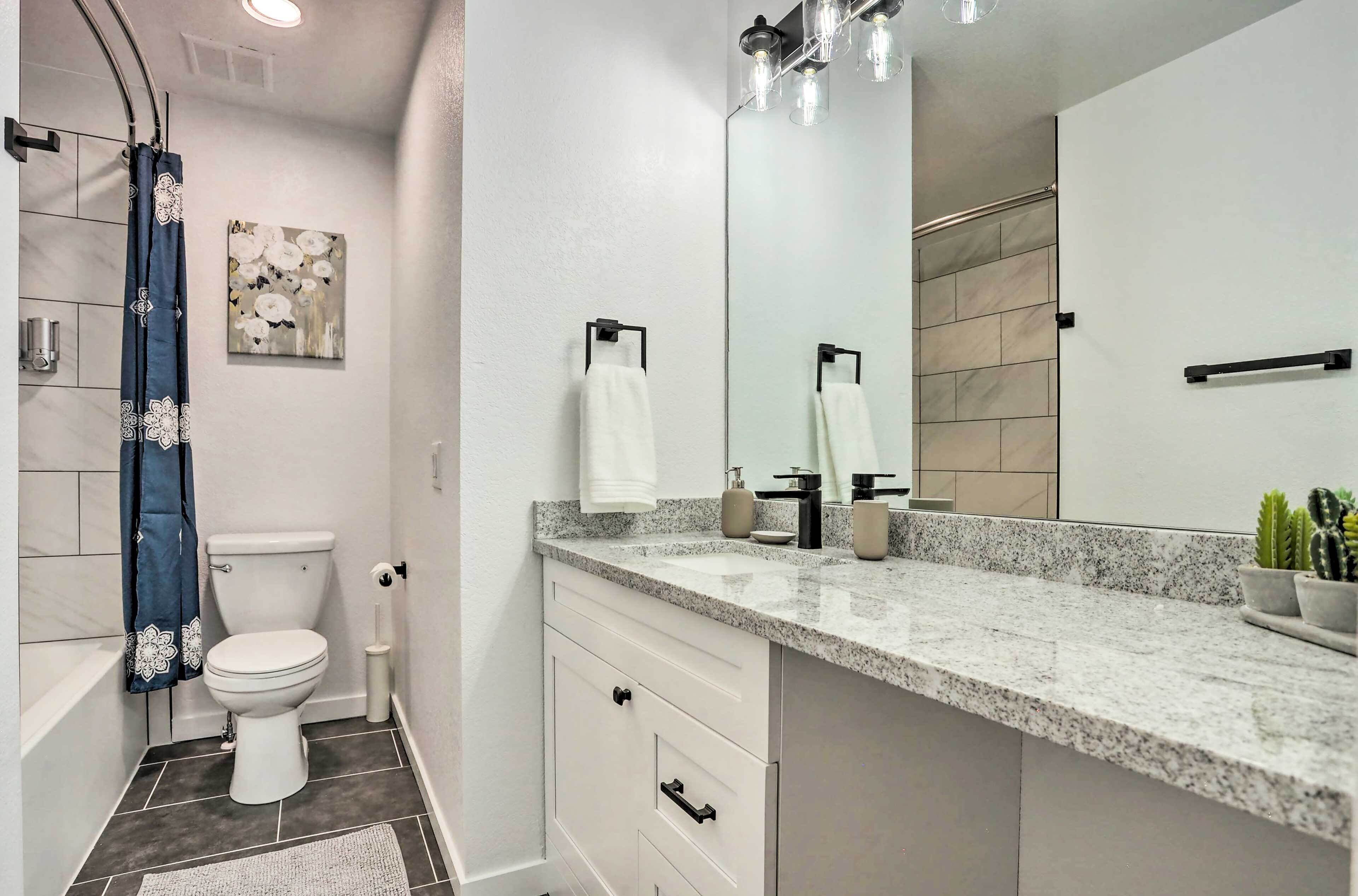 A modern bathroom with a white toilet, a large mirror, a granite countertop, and a shower curtain.