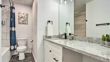 A modern bathroom with a white toilet, a large mirror, a granite countertop, and a shower curtain.