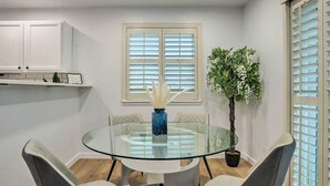 A dining area with a glass table surrounded by cushioned chairs, a potted plant, and a window with blinds. - 13 Mi to Dtwn Denver: Northglenn Townhome w/ Patio (Northglenn)