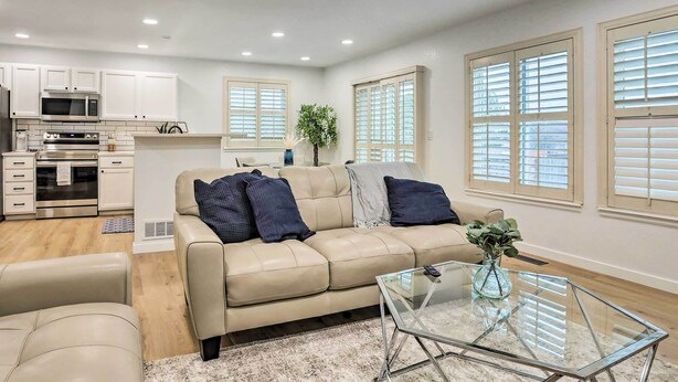 A modern living room with a beige sofa, a glass coffee table, and a kitchen area with white cabinets and appliances. - 13 Mi to Dtwn Denver: Northglenn Townhome w/ Patio (Northglenn)