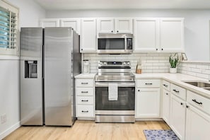 Une cuisine moderne avec des meubles blancs, des appareils en acier inoxydable, notamment un réfrigérateur, un four à micro-ondes et un four, ainsi qu’un petit espace de comptoir doté d’un évier et d’objets décoratifs.