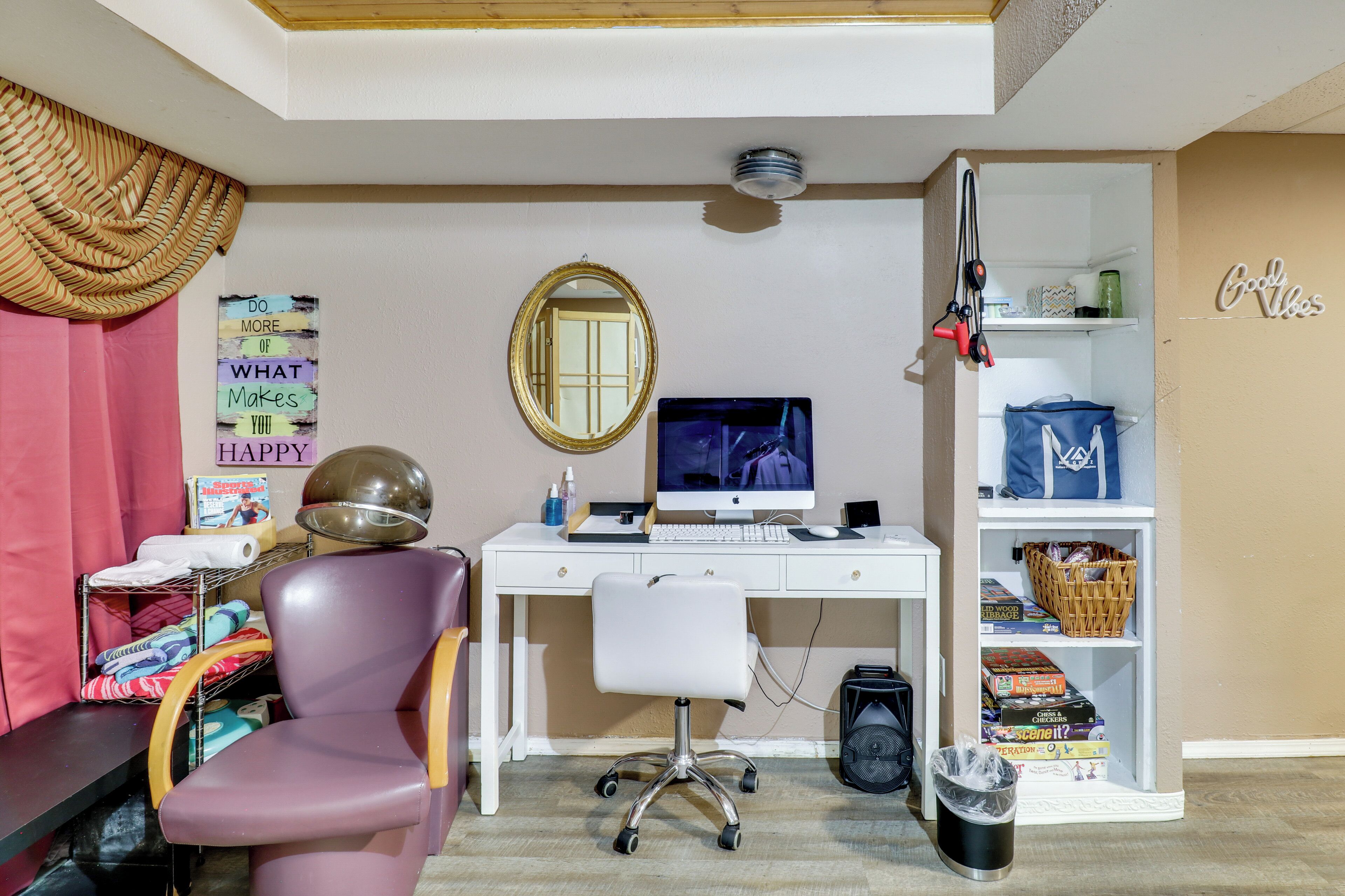 A room with a desk, chair, computer, and shelves with various items.
