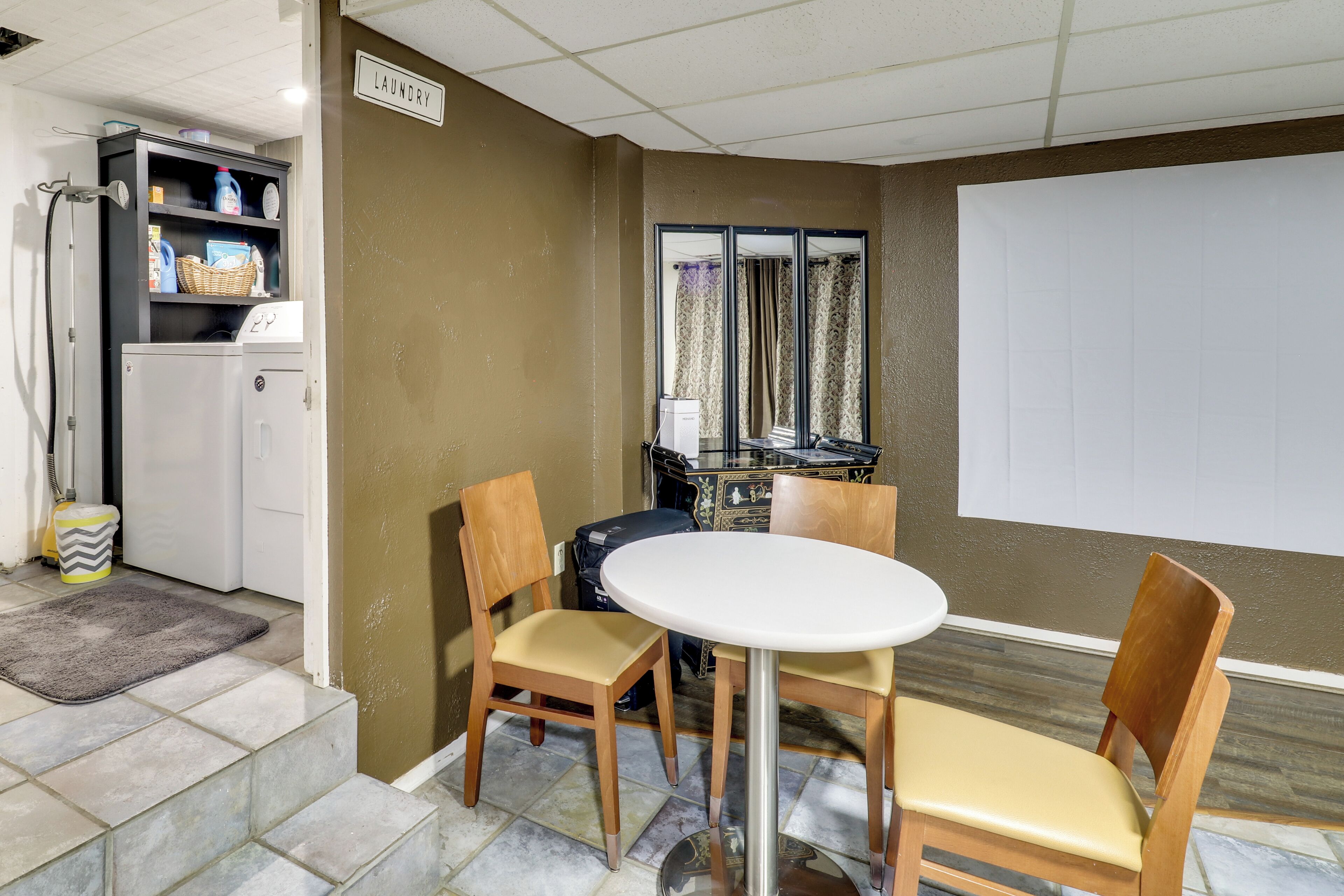 A compact living space with a kitchenette, a dining area with a table and chairs, a large mirror, and a laundry sign on the wall.