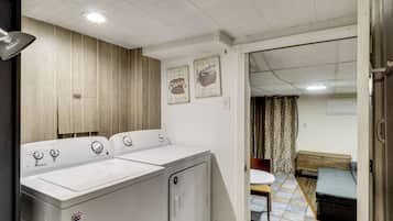 Un cuarto de lavandería con dos lavadoras blancas, paneles de madera en las paredes y un comedor visible a través de una puerta abierta.