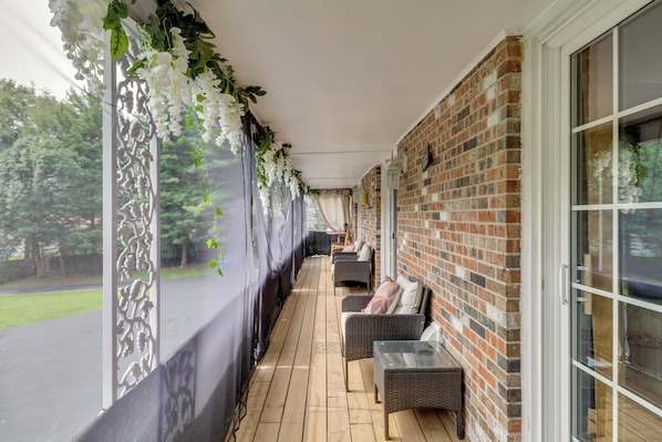 A covered outdoor seating area with wicker furniture and a brick wall.