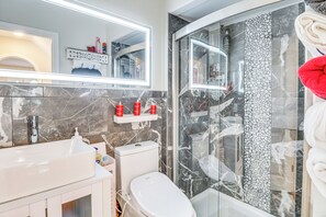 A modern bathroom with a white sink, toilet, and shower. There are red bottles on the shelf above the toilet and a towel rack with a red towel.