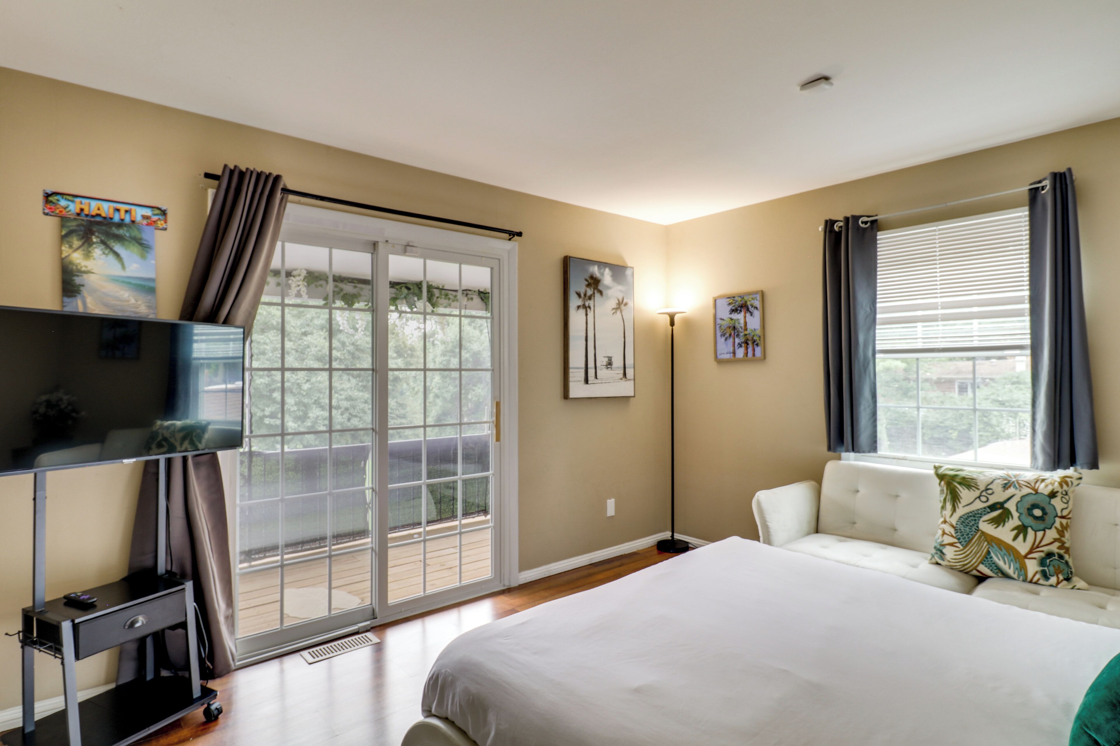 A bedroom with a large bed, a desk, a chair, a sofa, and a window with curtains.