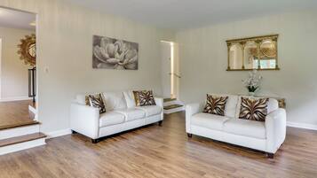 A spacious living area with two white sofas, a large floral painting, and a mirror with an ornate frame.