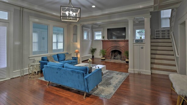 A spacious living room with a blue sofa, a fireplace, and a staircase leading to an upper level. - Beautifully Renovated Beach House w/ Fenced Patio! (Atlantic City)
