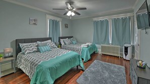 A bedroom with two beds, a ceiling fan, a radiator, and a TV. - Beautifully Renovated Beach House w/ Fenced Patio! (Atlantic City)