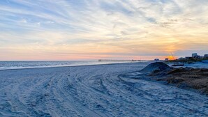 A beach with a pier extending into the water, sandy terrain, and a sunset in the background. - Beautifully Renovated Beach House w/ Fenced Patio! (Atlantic City)