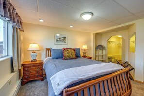 A bedroom with a bed, two bedside tables with lamps, a dresser, a window with curtains, a painting on the wall, and a closet with hanging clothes. - Anchorage Apt: Home Base for Alaska Adventure! (Anchorage)