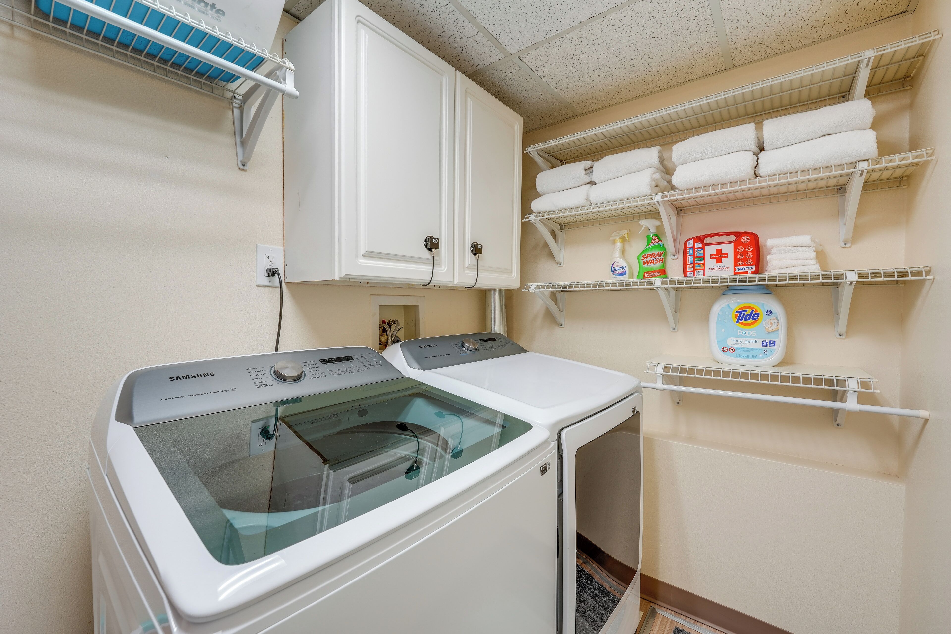 A laundry area with a Samsung washer and dryer, shelves with folded towels, and laundry supplies.