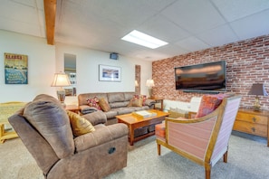 A living room with a brick wall, a flat-screen TV, a brown leather sofa, a wooden coffee table, and a patterned armchair. - Anchorage Apt: Home Base for Alaska Adventure! (Anchorage)