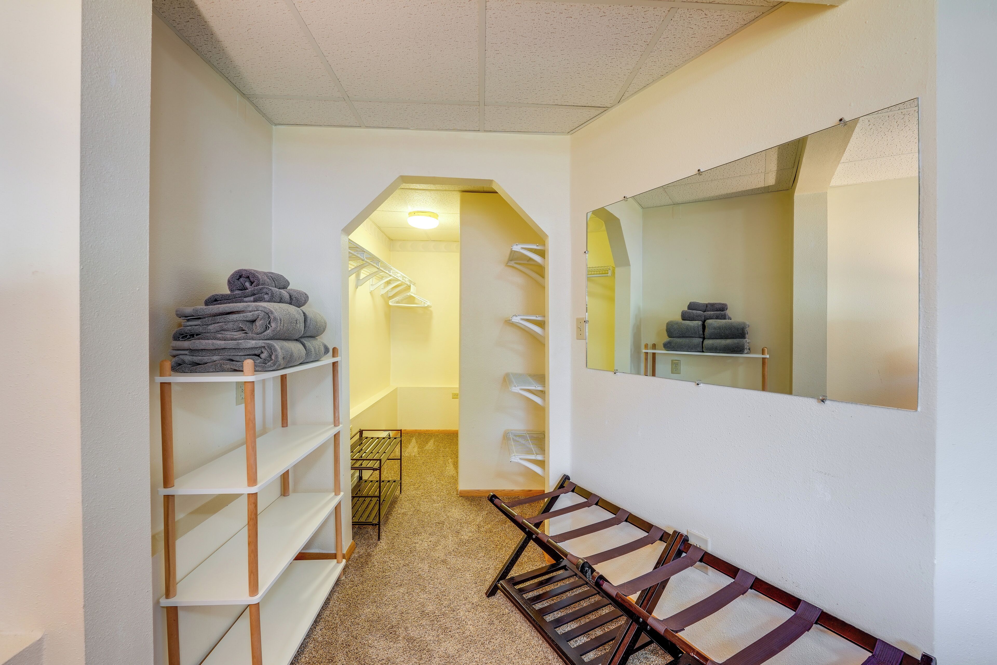 A narrow hallway with a wooden bench, a mirror, and shelves with folded towels.