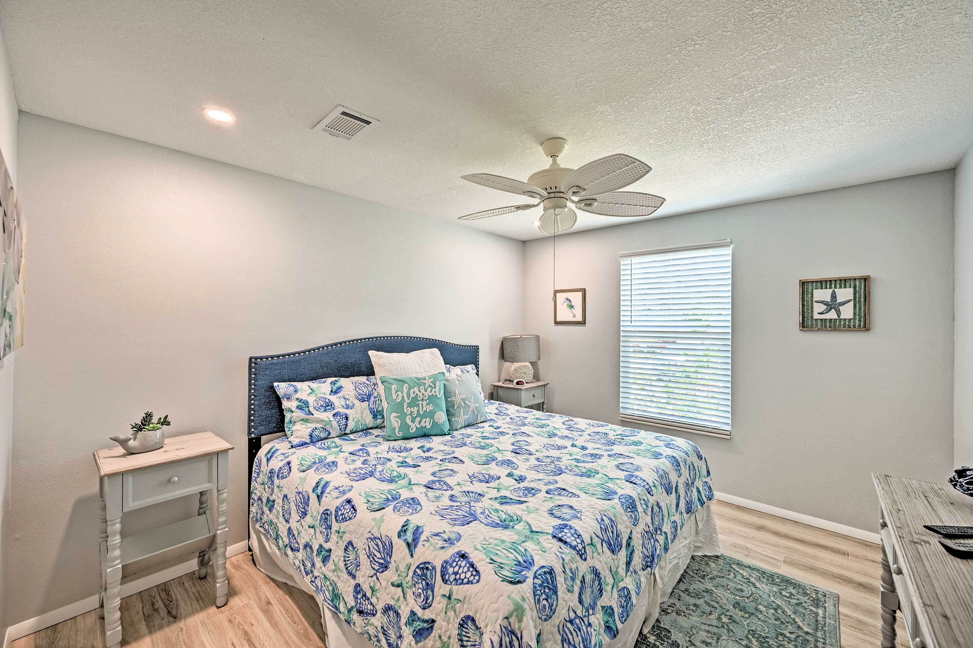 A bedroom with a bed, a nightstand, a ceiling fan, a window with blinds, and a framed picture on the wall.