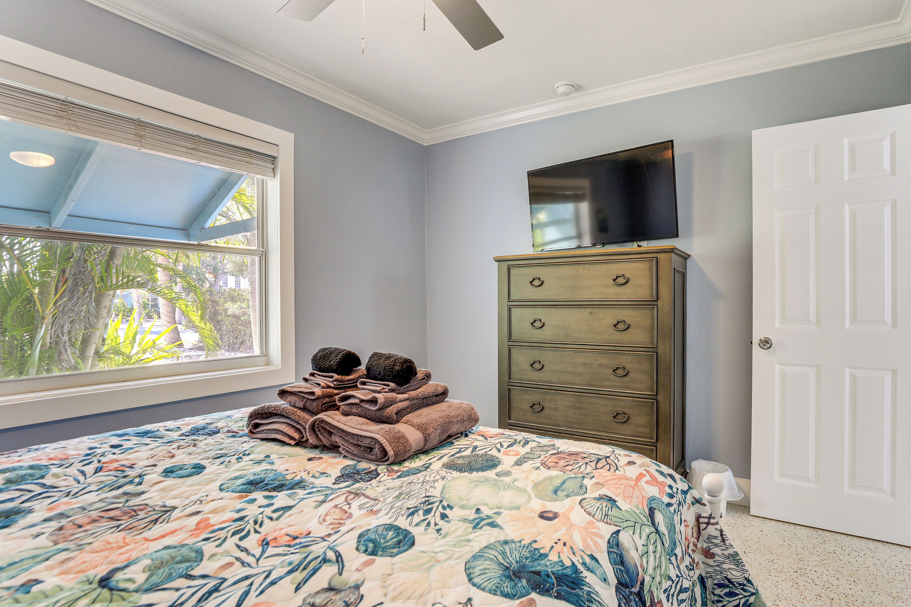 Une chambre à coucher comprenant un lit, une commode, un téléviseur et une fenêtre donnant sur un paysage verdoyant.