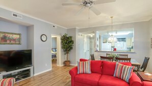 Ein Wohnzimmer mit rotem Sofa, Fernseher, Deckenventilator und einem Essbereich im Hintergrund.