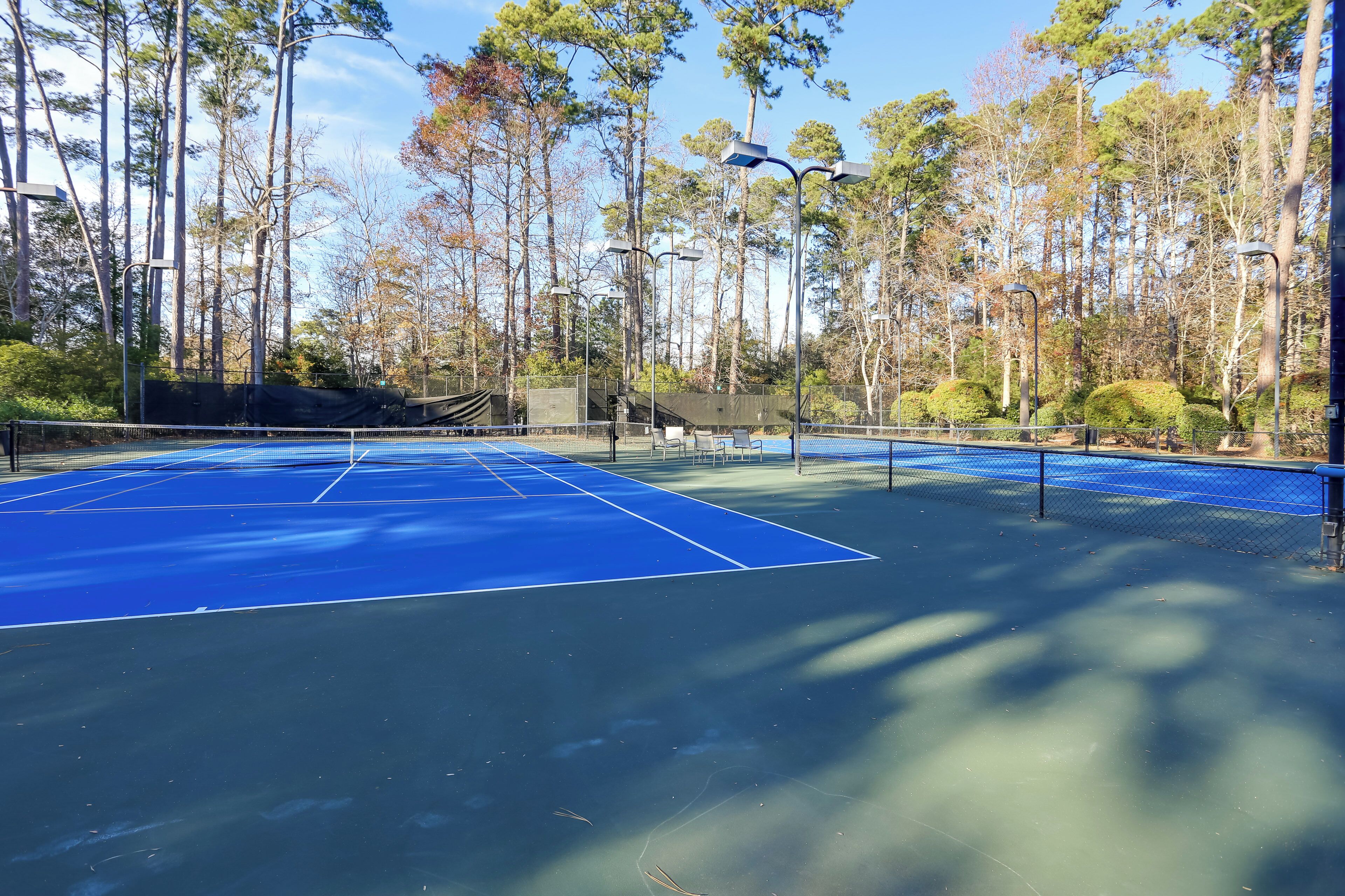 A tennis court with a blue surface, surrounded by trees and street lamps.