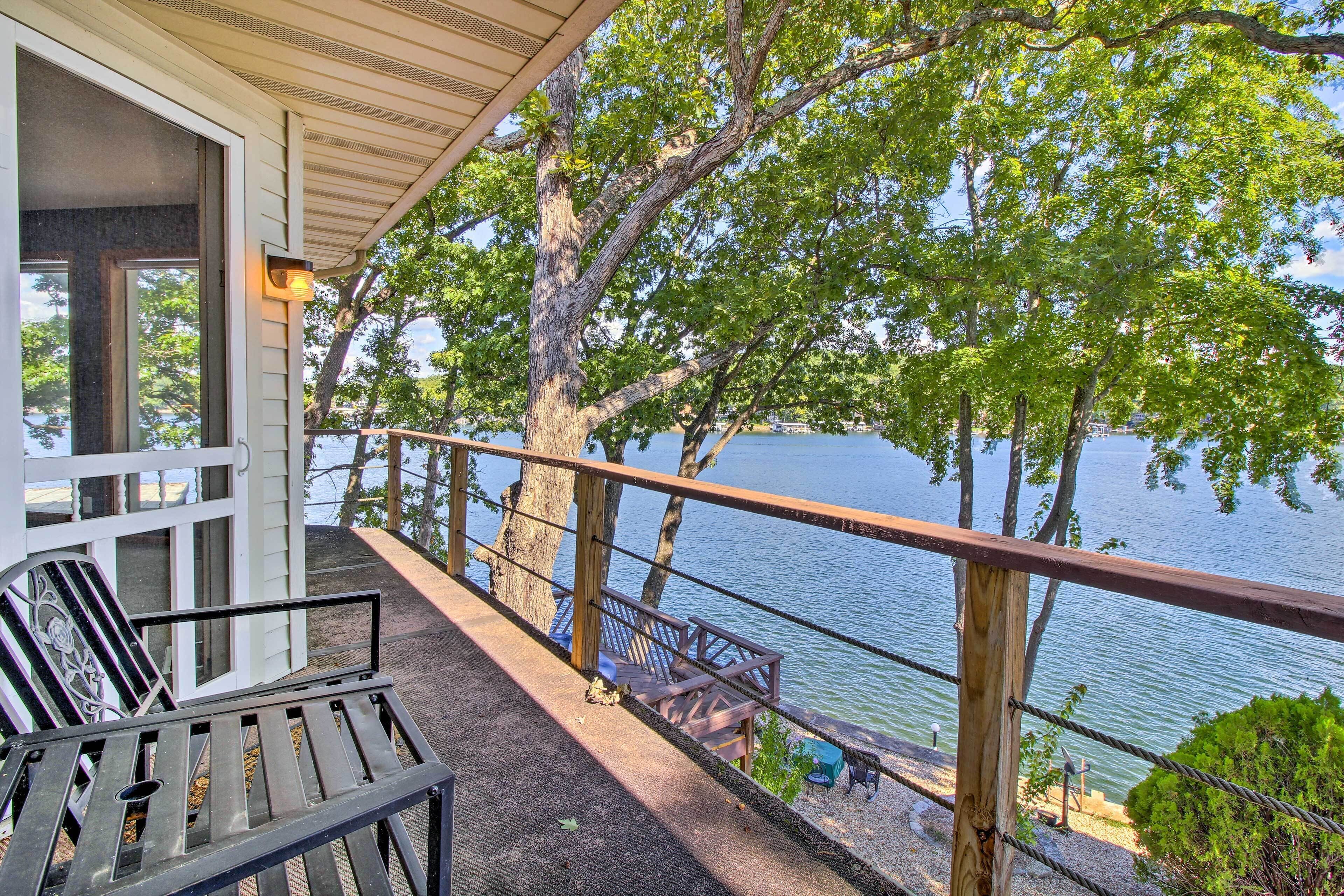 Un balcón con vistas a un lago, barandas de madera y mobiliario exterior.