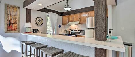 A modern kitchen with wooden bar stools, a white countertop, and built-in appliances.