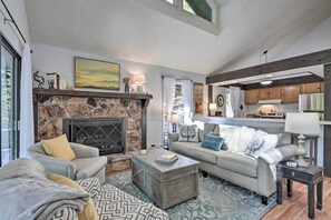A living room with a stone fireplace, a sofa, a coffee table, and a view into the kitchen. - Pools, Water Park! Margaritaville Resort Home (Osage Beach)