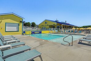 A pool area with lounge chairs, a lifeguard station, and a building with a blue roof. - Pools, Water Park! Margaritaville Resort Home (Osage Beach)