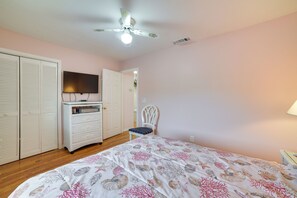 A bedroom with a bed, a TV, a wardrobe, a chair, and a ceiling fan. - Panama City Beach Townhome - Walk to Beach! (Panama City Beach)