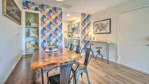 A dining area with a wooden table and chairs, a kitchen in the background, and a wall with a colorful floral pattern. - Cozy Branson Retreat w/ Balcony, 2 Mi to 76 Strip (Branson)