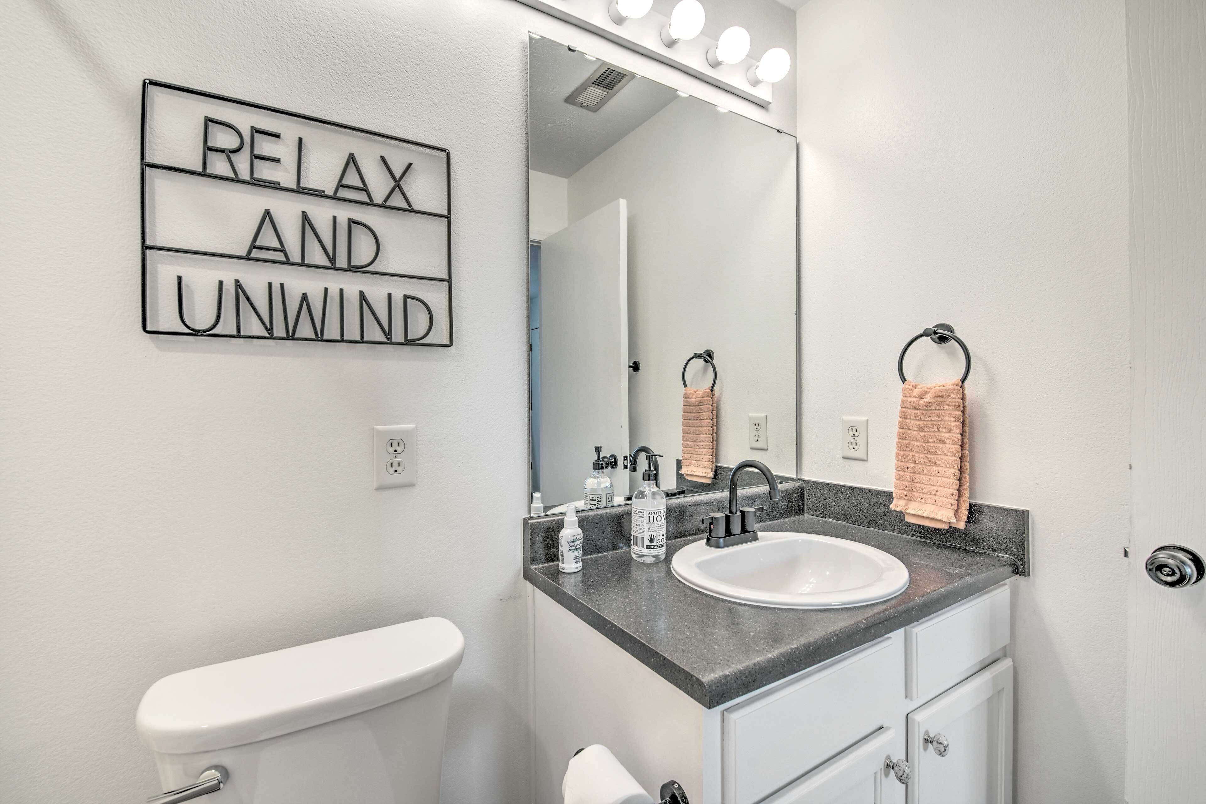 Een badkamer met een wit toilet, een wastafel met een spiegel erboven en een bordje met de tekst 'RELAX AND UNWIND'.