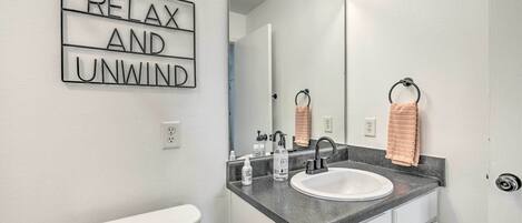 Een badkamer met een wit toilet, een wastafel met een spiegel erboven en een bordje met de tekst 'RELAX AND UNWIND'.
