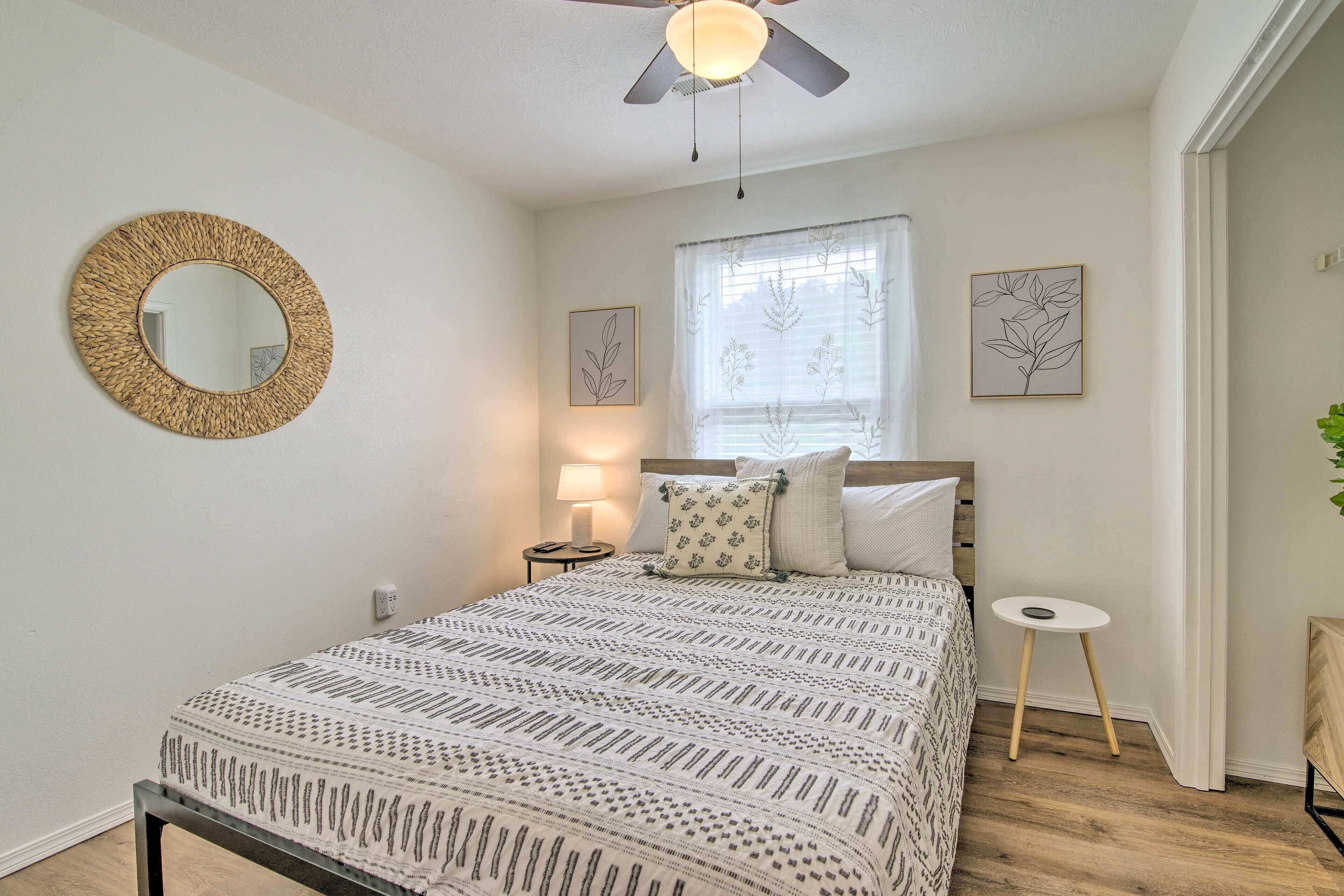 Une chambre avec un lit, un miroir rond, une fenêtre avec des rideaux et une petite table.