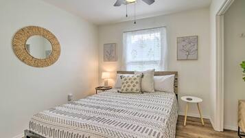 Une chambre avec un lit, un miroir rond, une fenêtre avec des rideaux et une petite table.