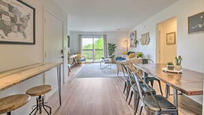 A spacious living area with a long wooden table, multiple chairs, a sofa, and a coffee table. There is a large window with a view of greenery outside. - Cozy Branson Retreat w/ Balcony, 2 Mi to 76 Strip (Branson)