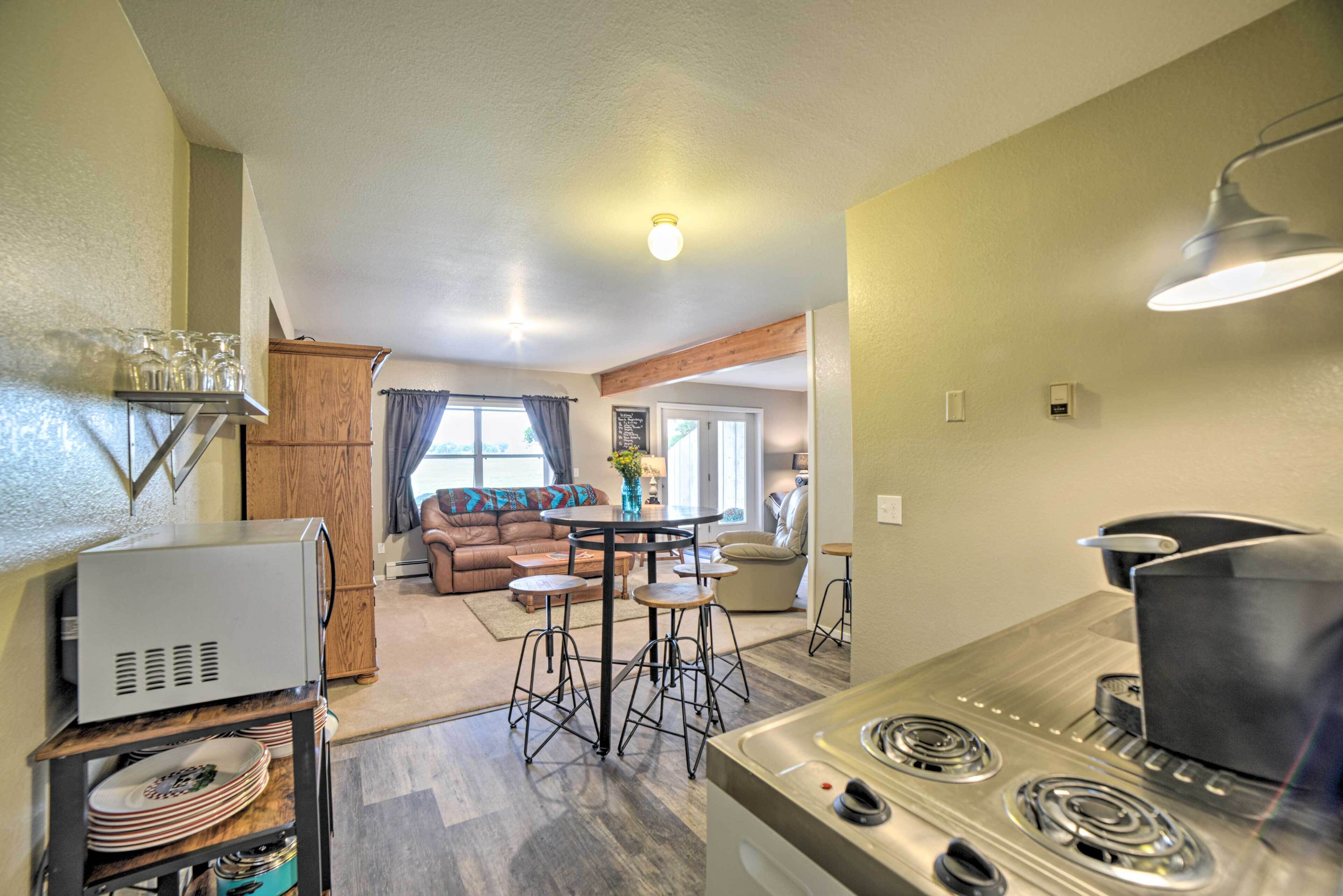 A compact kitchen with a stove, bar stools, and a dining table. A living area with a sofa and a coffee table is visible in the background.