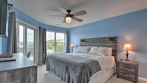 A bedroom with a large bed, a ceiling fan, a nightstand with a lamp, and a view of the outdoors through a window. - 'the Lake Escape w/ Balcony & Pool Access! (Camdenton)