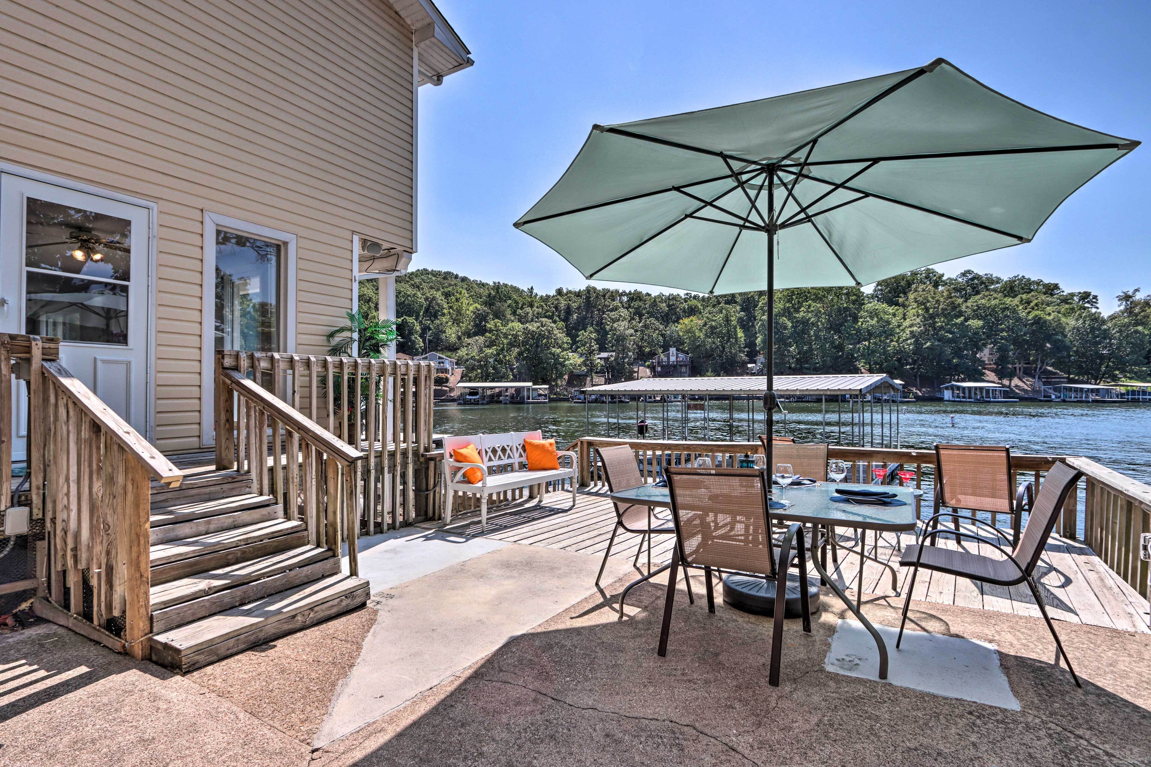 A deck with outdoor furniture, a large umbrella, and a view of a lake with boats.