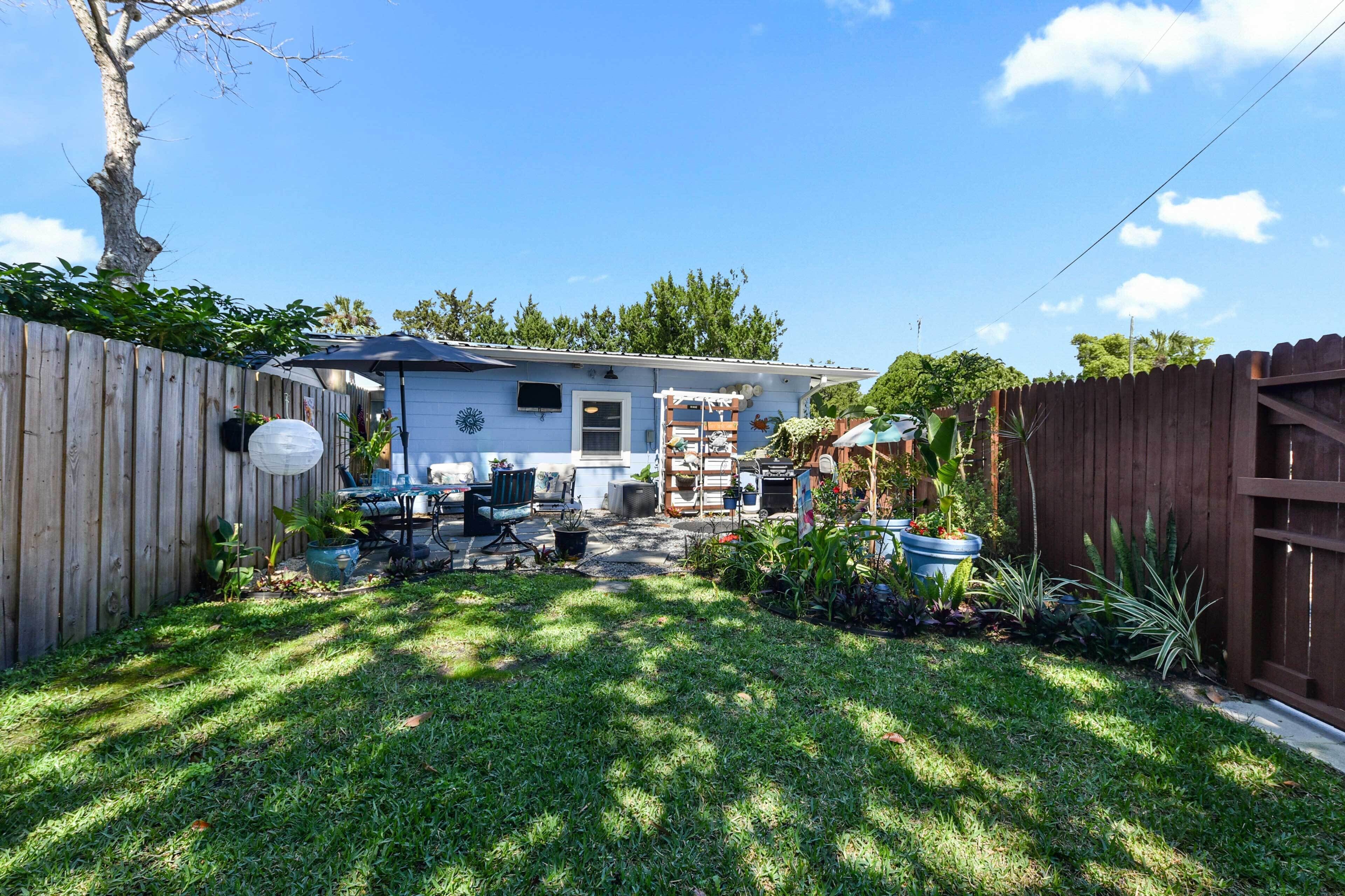 A backyard with a wooden fence, a patio area with outdoor furniture, and various potted plants.