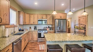 Une cuisine moderne avec des meubles en bois, des appareils électroménagers en acier inoxydable, des plans de travail en granit et des luminaires suspendus.