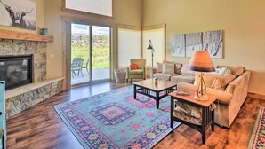 Un salon spacieux avec une cheminée en pierre, une grande fenêtre, un canapé, une table basse et un tapis à motifs.