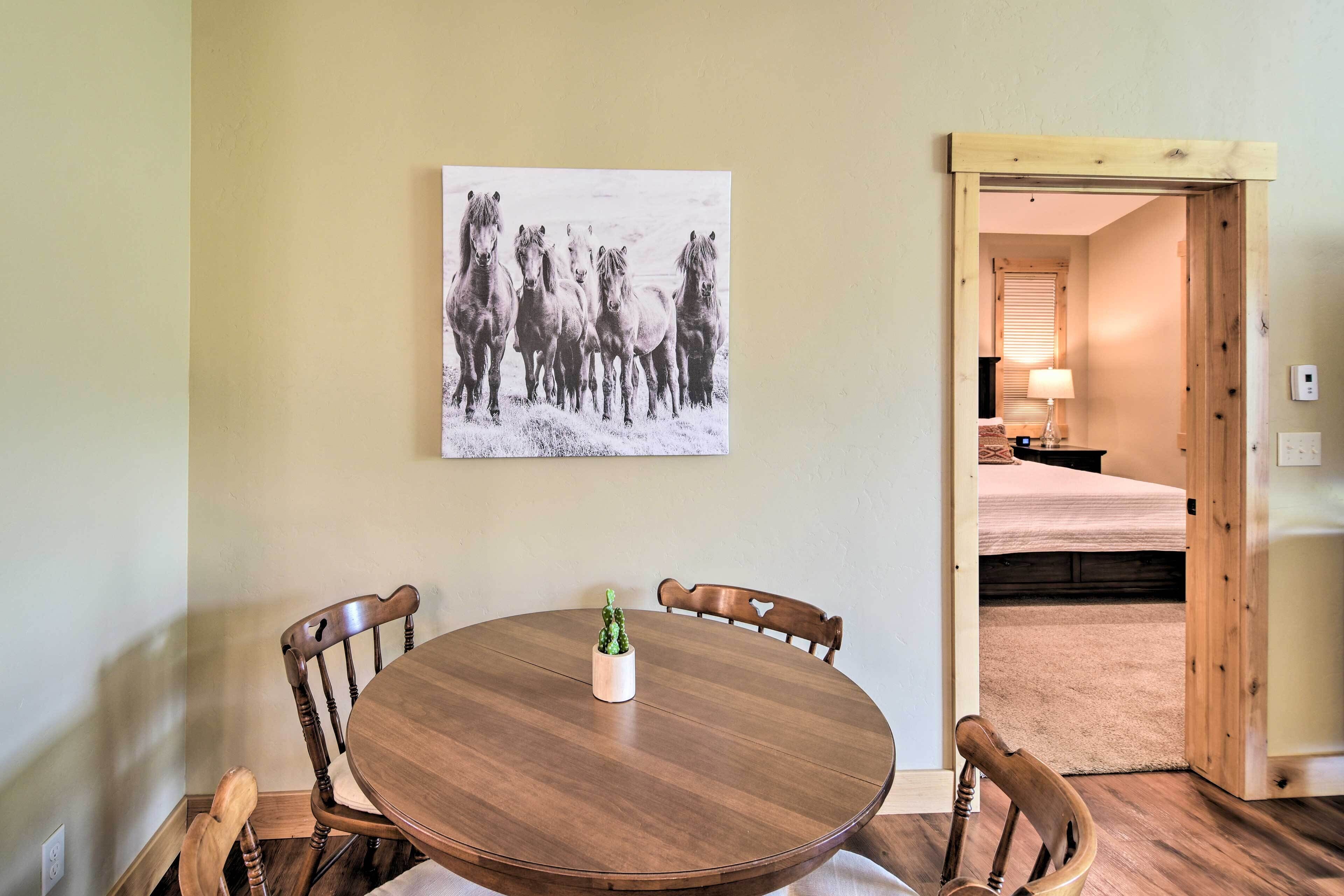 Un comedor con una mesa redonda de madera, cuatro sillas y un cuadro de caballos colgado en la pared.