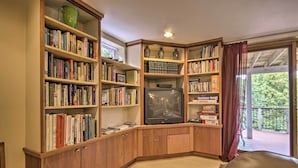 A corner room with wooden bookshelves filled with books, a television, and a window with a view of greenery. - Harpers Ferry Apartment w/ Private Pool & Hot Tub! (Harpers Ferry)