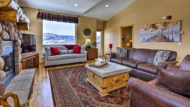 A cozy living room with a fireplace, a large window with a mountain view, a brown leather sofa, and a patterned rug. - 11 Mi to Keystone: Silverthorne Condo w/ Deck (Silverthorne)