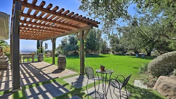 Relax in a serene patio area with a pergola, seating, and lawn, surrounded by mature trees.