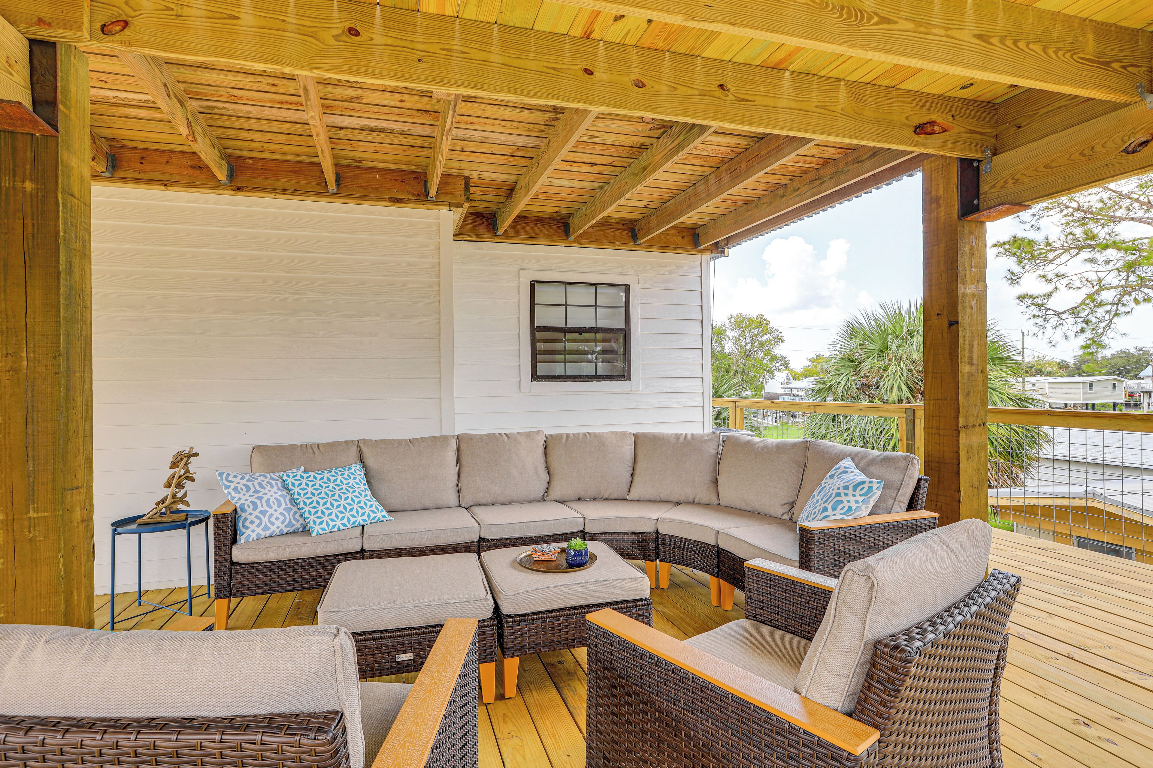 A covered outdoor seating area with a curved sectional sofa, wicker chairs, and a small table with a tray.